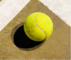 Tennis ball resting on the corner of a clay court line
